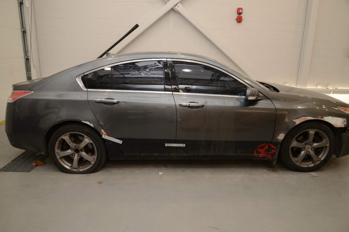 A side view of a grey sedan vehicle with a decal of a red star and skull on the bottom front passenger door.