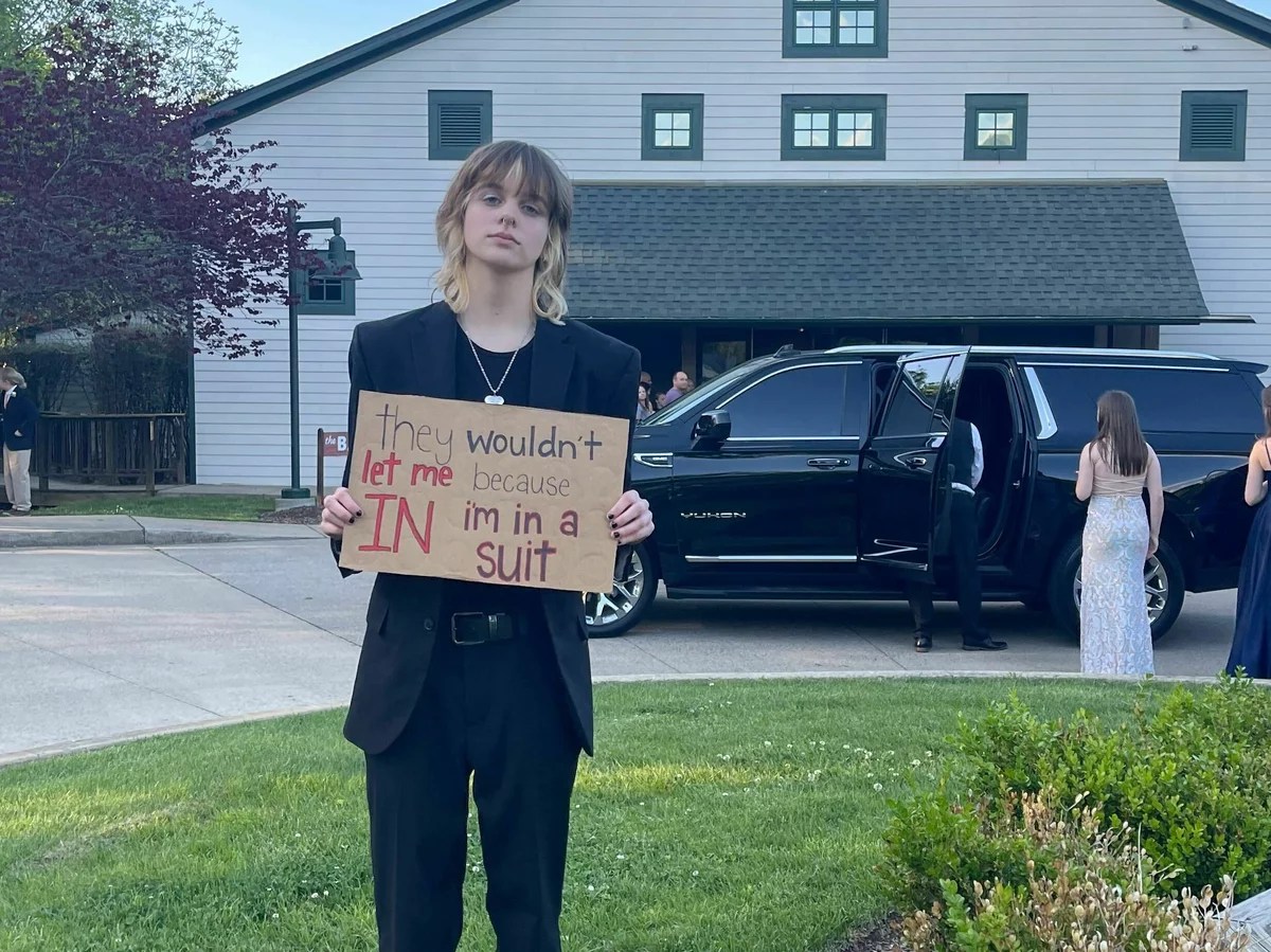 B Hayes holding a sign that reads, "they wouldn't let me in because i'm in a suit."
