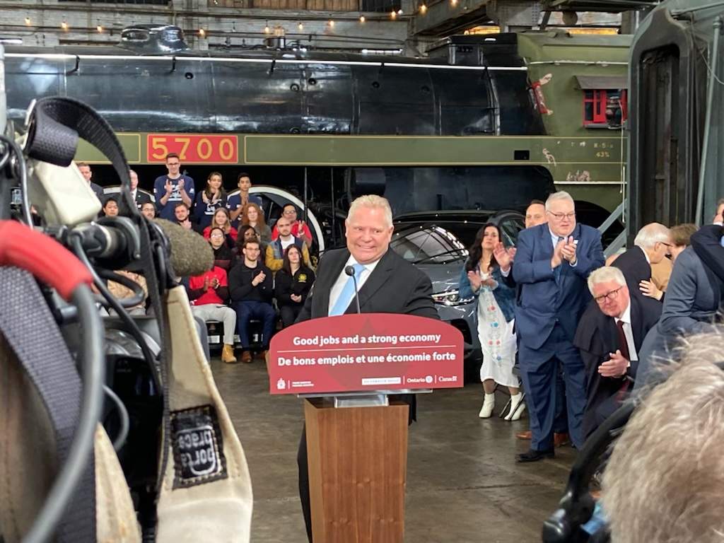 Premier Doug Ford stands at a podium in front of a railway car at a museum in St. Thomas, Ont.