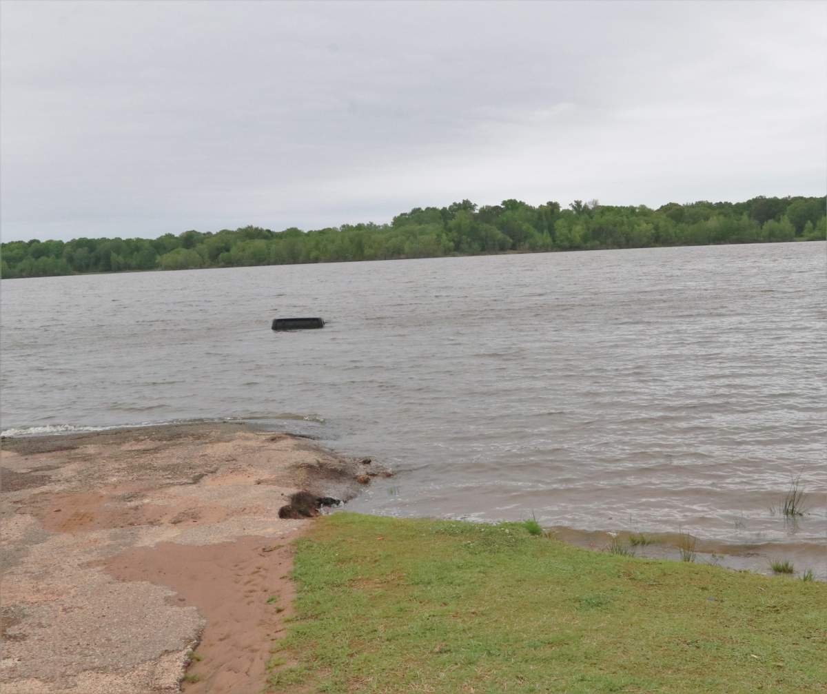 Photo of a black Jeep submerged underwater with only a small portion of its roof still visible above the surface of Lake o' the Pines in east Texas.