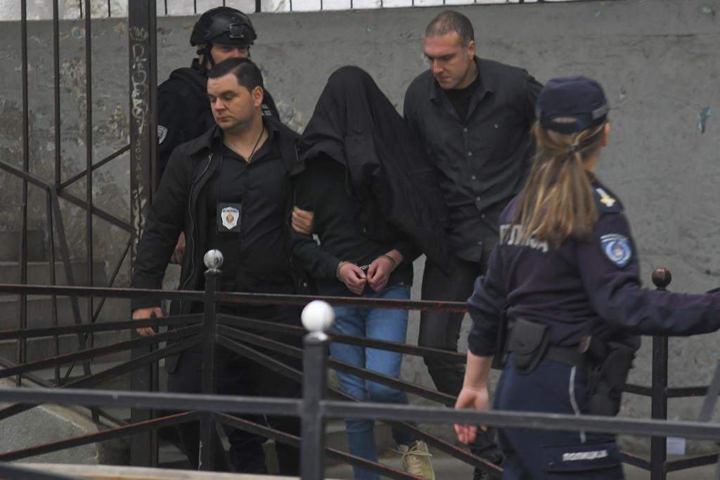 A suspect is escorted by police outside the Vladislav Ribnikar school in Belgrade, Serbia, Wednesday, May 3, 2023. Serbian police say a teenage boy opened fire at a school in central Belgrade, killing several people and injuring several more. (AP Photo)