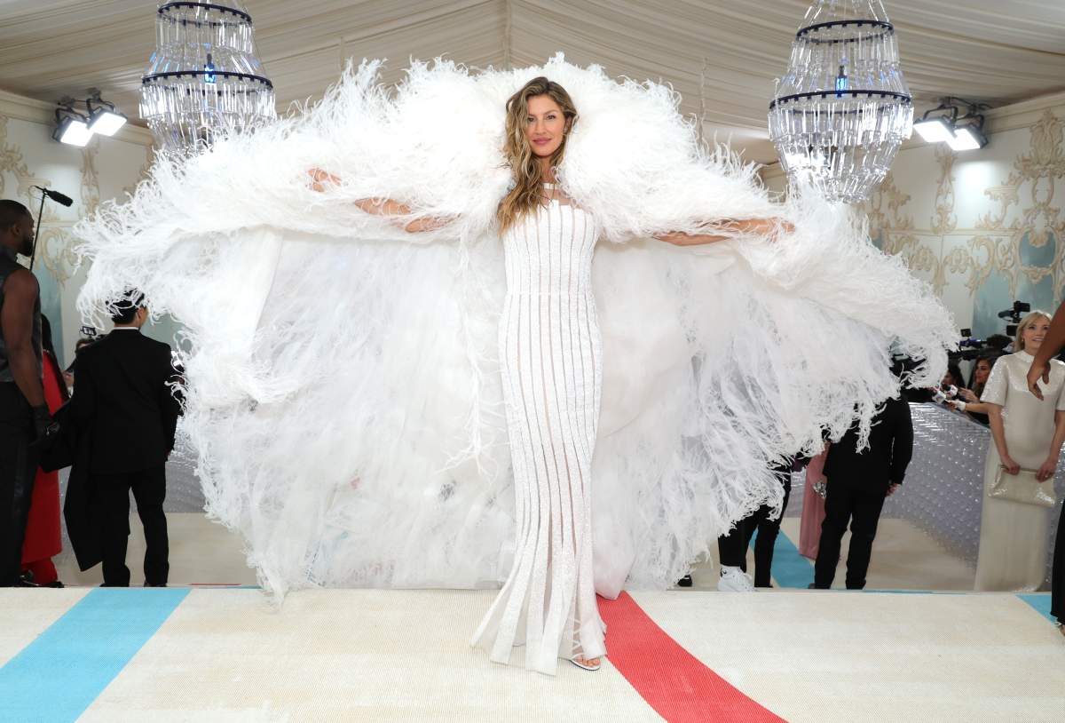 Gisele Bündchen in a full-length white dress with a massive feather cape behind her.