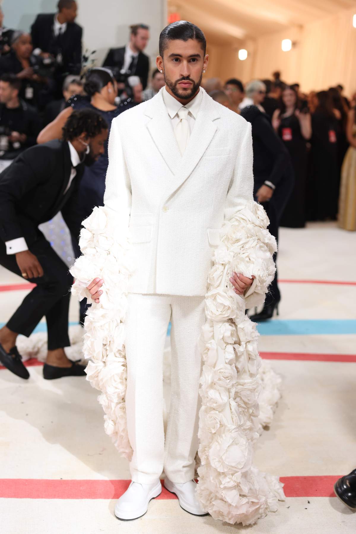Bad Bunny wearing a white suit with billowing white rose sleeves. His hair is gelled down.