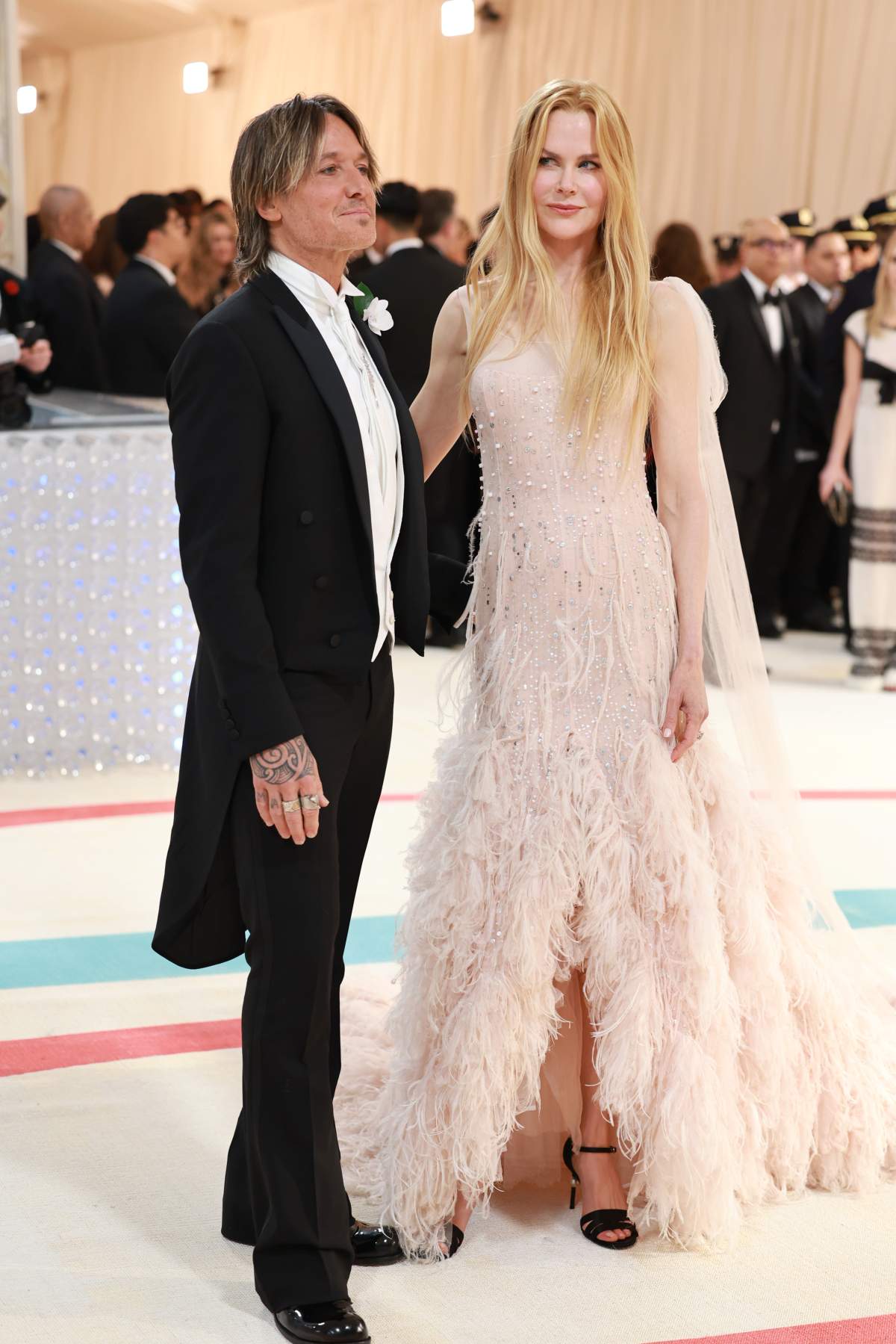 Nicole Kidman wears a floor-length pink, feathered dress. Keith Urban wears a black tuxedo,
