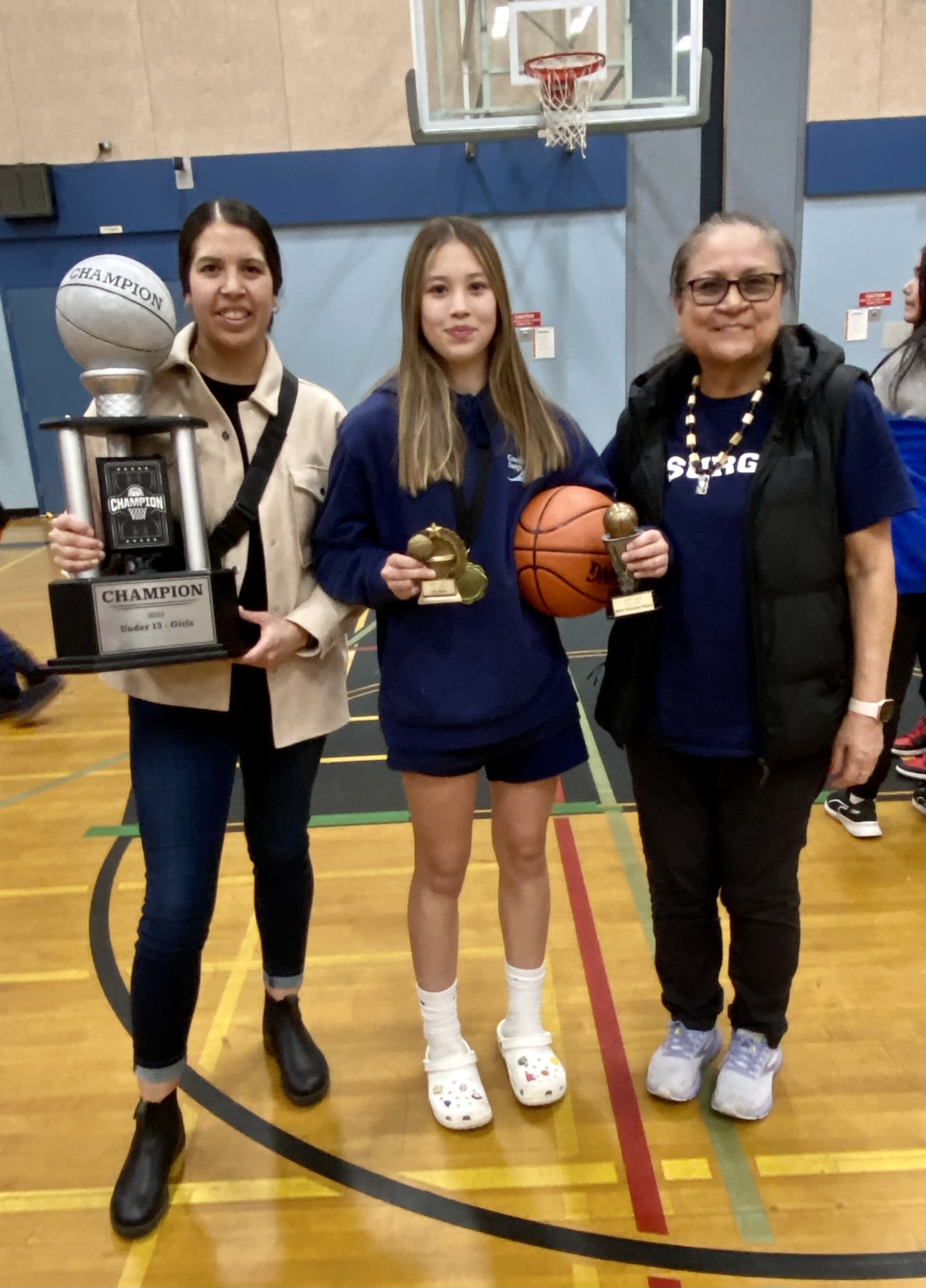 Three generations of women stand together, one holds a trophy, another a basketball.