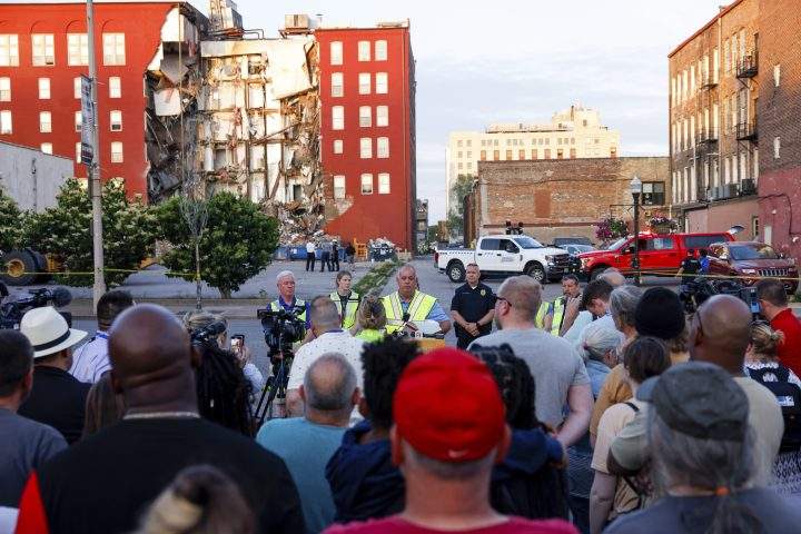 A multi-storey apartment building sits with a section missing, exposing units inside, following a partial collapse of the structure