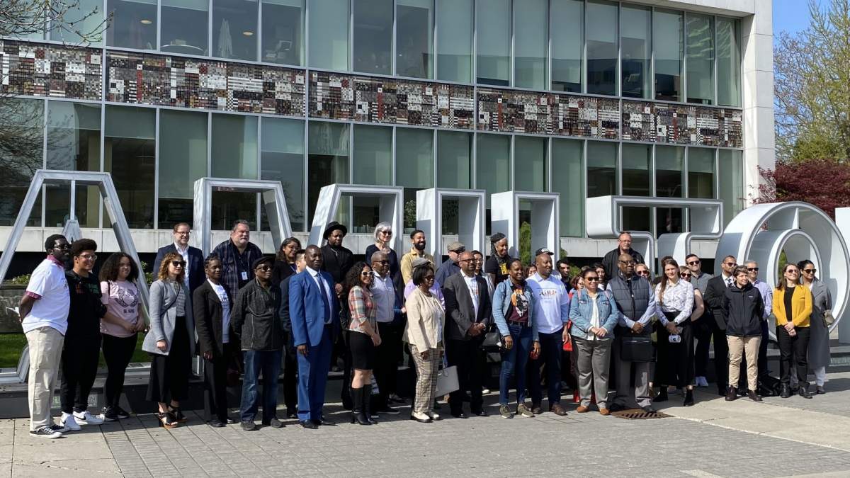 A group of anti-hate advocates gathers in front of the Hamilton sign in front of Hamilton City Hall.