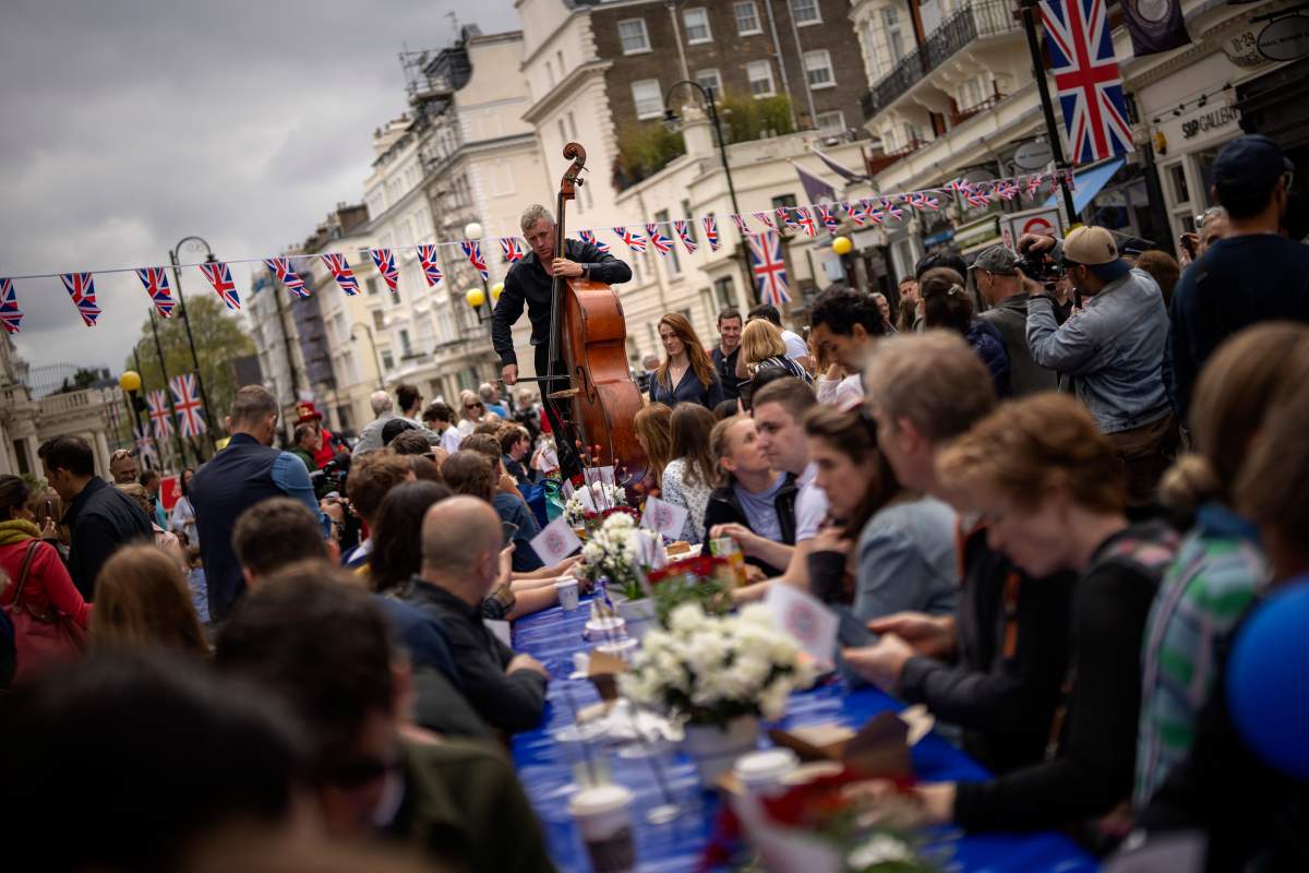 A musician plays his double bass as people sit at long tables to eat their lunch as part of the Big Lunch celebration in London, Sunday, May 7, 2023. The Big Lunch is part of the weekend of celebrations for the Coronation of King Charles III. (AP Photo/Emilio Morenatti)