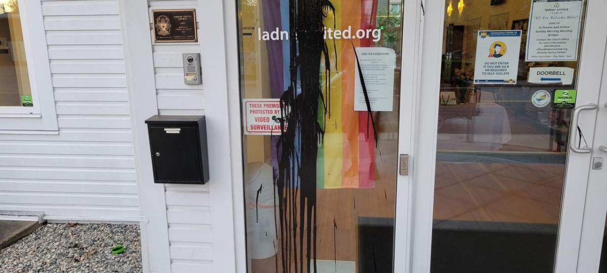 Black paint can be seen splashed over a Pride flag behind glass at the Ladner United Church on Wednesday.