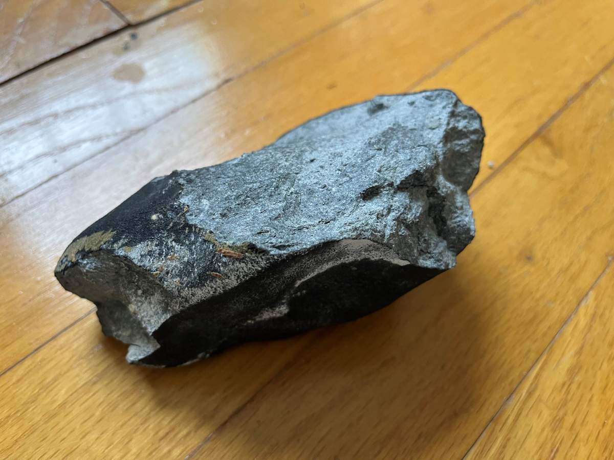 Another angle of the meteorite. It is greyish, jagged and shiny.