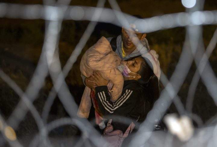 A migrant couple struggle while carrying their baby as they approach a gate in the border fence after crossing from Ciudad Juarez, Mexico into El Paso, Texas, in the early hours of Thursday, May 11, 2023.