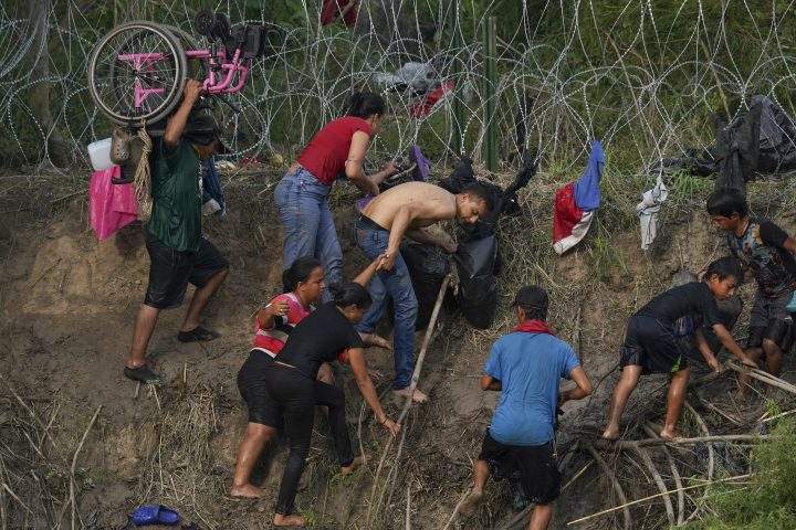 Colombian migrant Mireya Payares, centre in black, who has been forced to use a wheelchair during her trip north, is helped by another migrant to cross the Rio Grande river from Matamoros, Mexico, Wednesday, May 10, 2023.