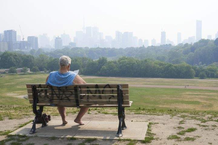 A person sits on a bench overlooking Riverdale Park East in Toronto on June 6, 2023, as the city remains under a special air quality statement caused by forest fires.