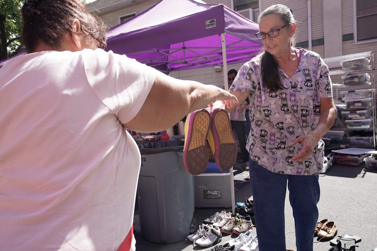 A woman handing shoes to someone in front of a purple tent.