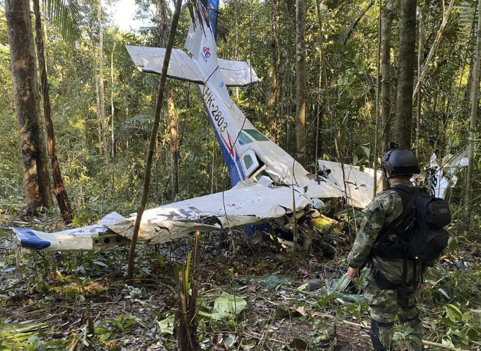 A soldier stands in front of a small, crashed airplane.