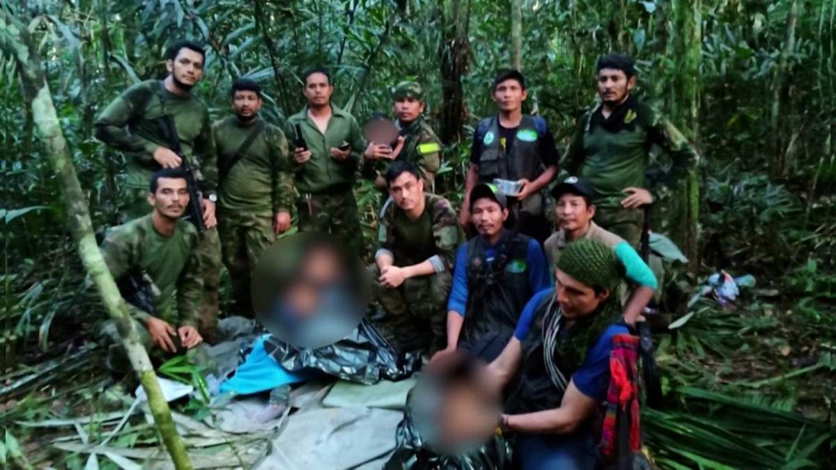 The four children, three of whom are wrapped in thermal blankets, pose with men in military uniforms and civilian clothes. The infant is in the arms of a solider.
