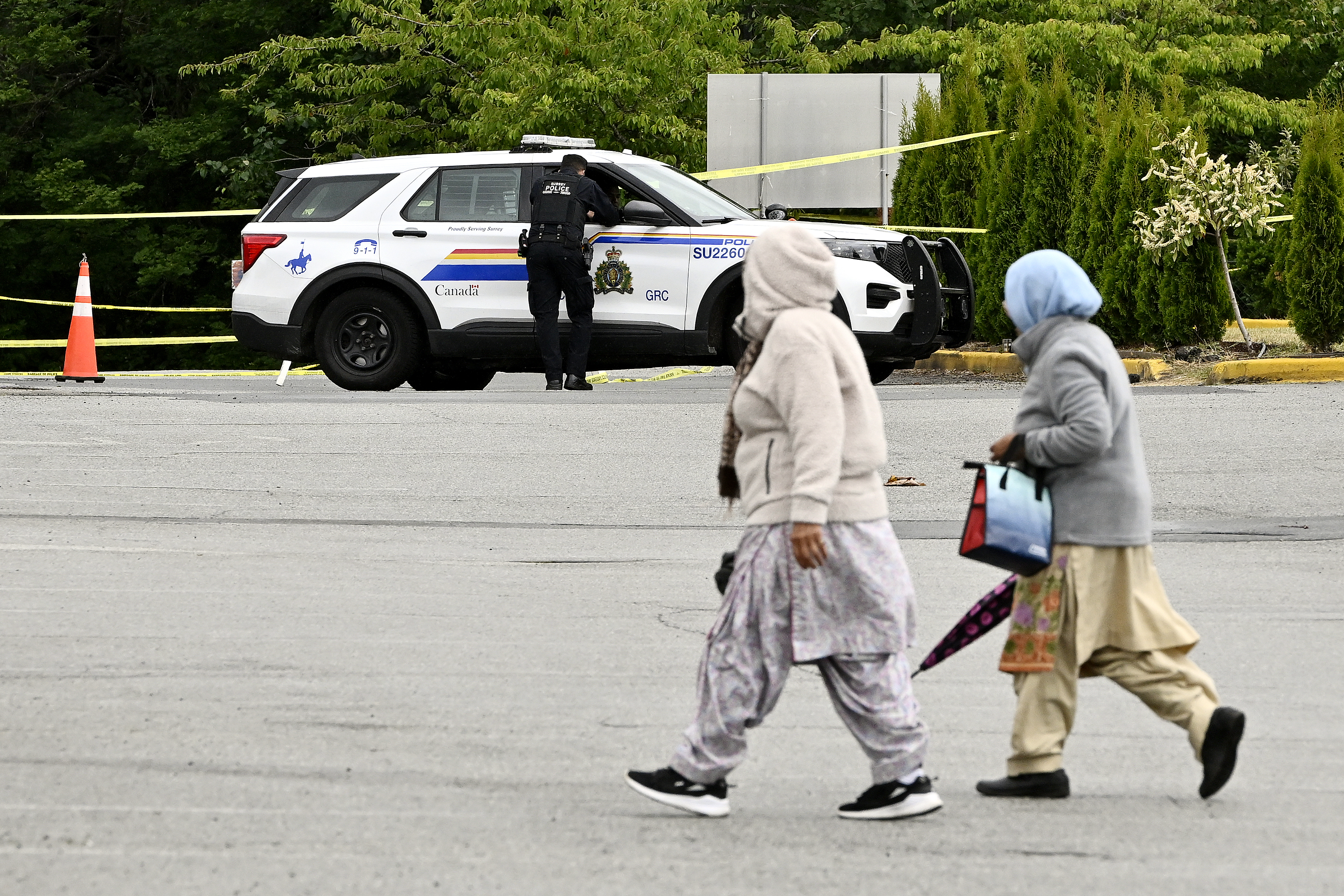 Community members walk past police vehicles outside of the Guru Nanak Sikh Gurdwara Sahib temple, in Surrey, B.C., on Monday. THE CANADIAN PRESS/Jennifer Gauthier.