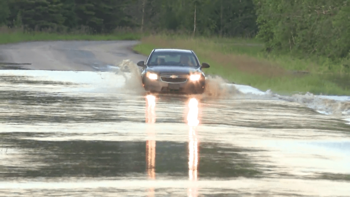A car drives over a flooded road in Woodlands County, Alta.