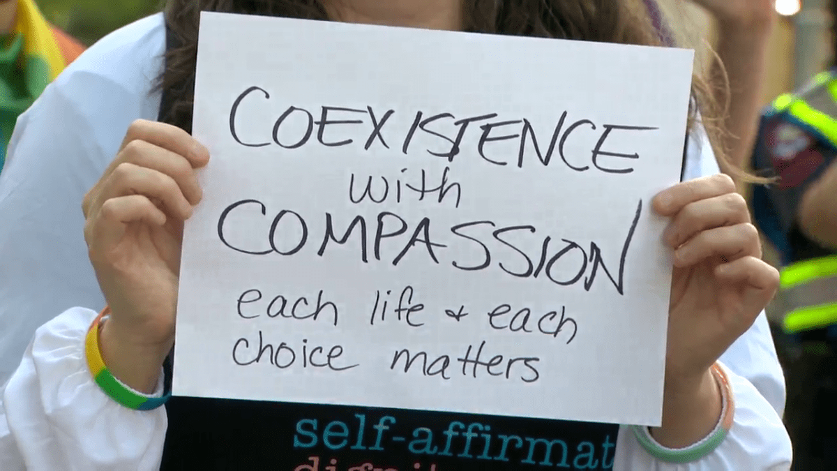 A counter-protestor holds up a sign at an anti-LGBTQ2 protest in Calgary on June 24, 2023.