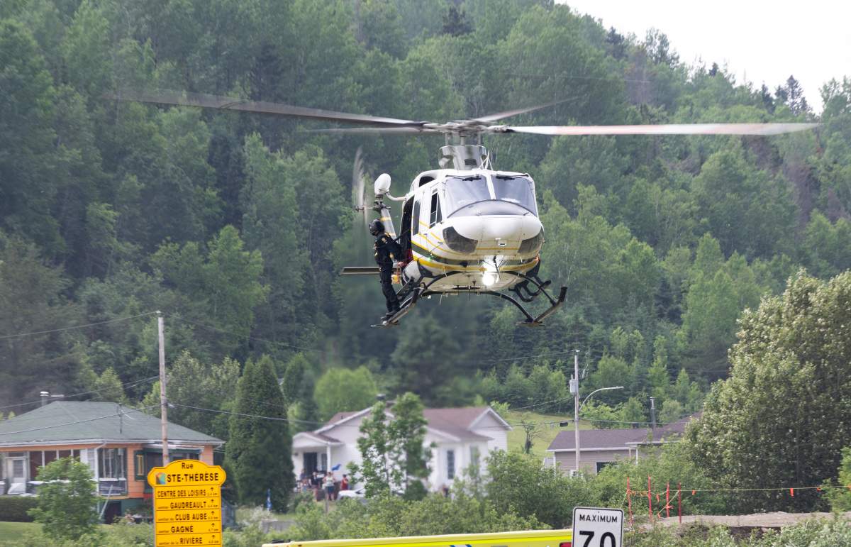 A police officer hangs from the side of the helicopter as they head to an isolated area to conduct rescue operations in Riviere-Eternite, Que., Sunday, July 2, 2023. A major landslide caused by heavy rain cut highway 170 between Saguenay, Que., and Saint-Simeon. Two people are missing after they were swept from the road by flood waters.
