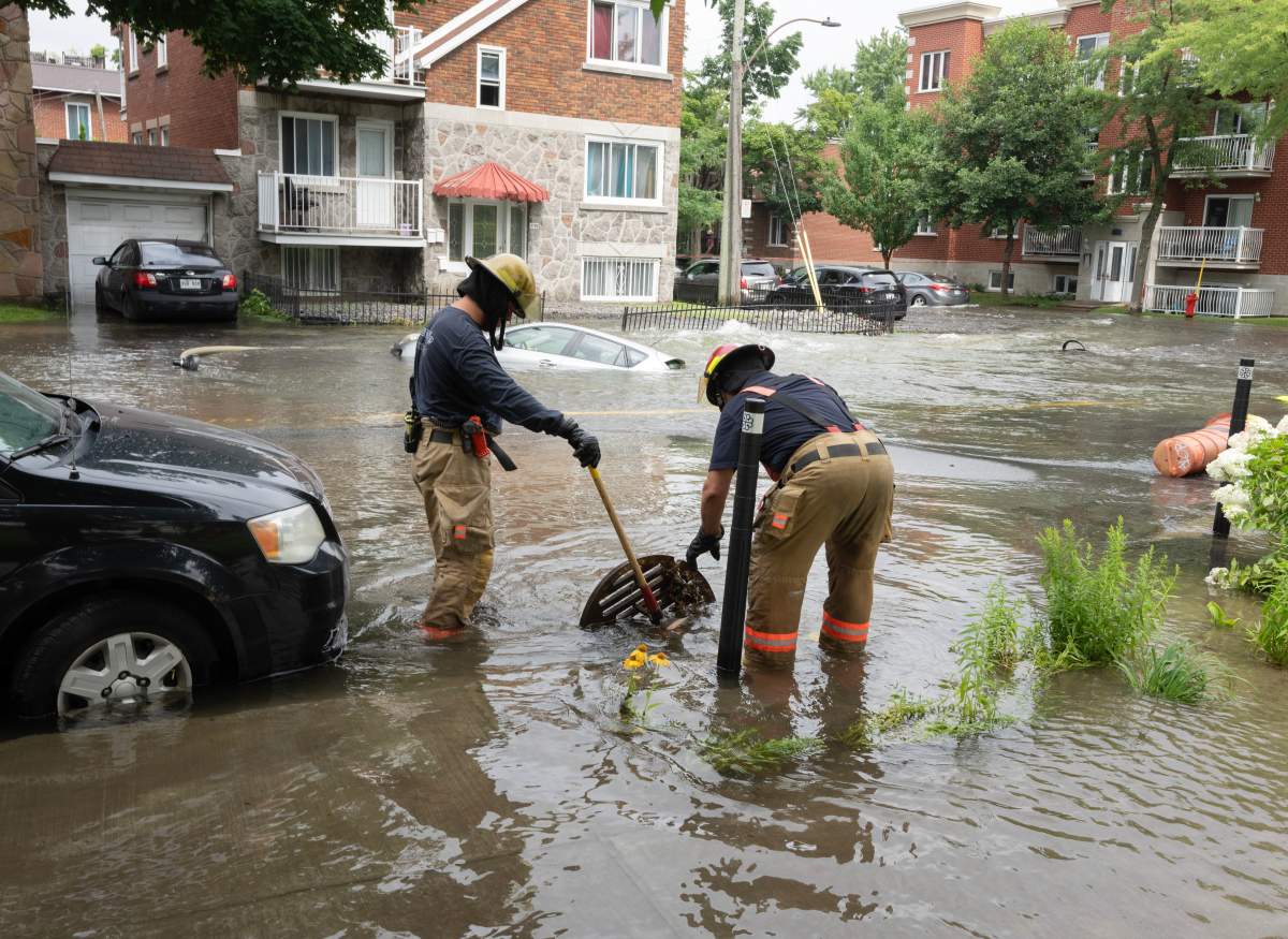 Firefighters remove a manhole cover after a water main broke flooding several blocks Friday, July 28, 2023 in Montreal.