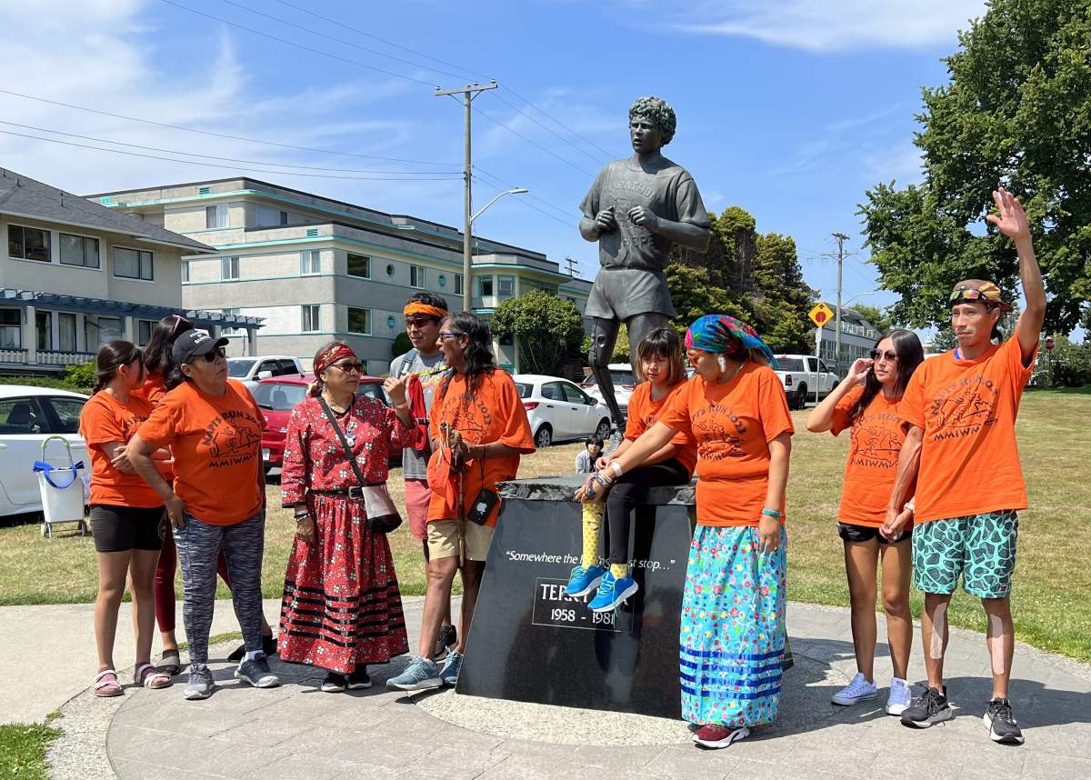 A group of people wearing orange stand in front of the Terry Fox statue
