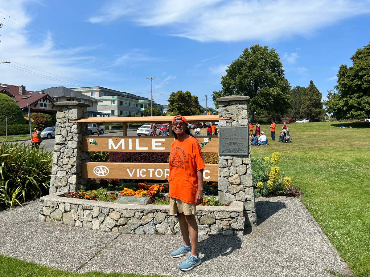 A man wearing orange stands in front of the Mile 0 marker in Victoria, B.C.