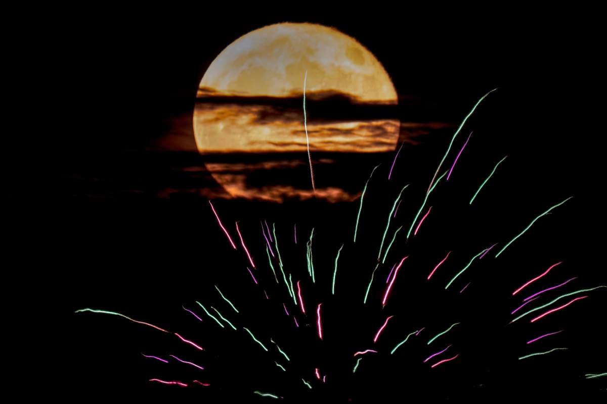 The buck supermoon rises behind fireworks Monday in Kansas City, Mo.