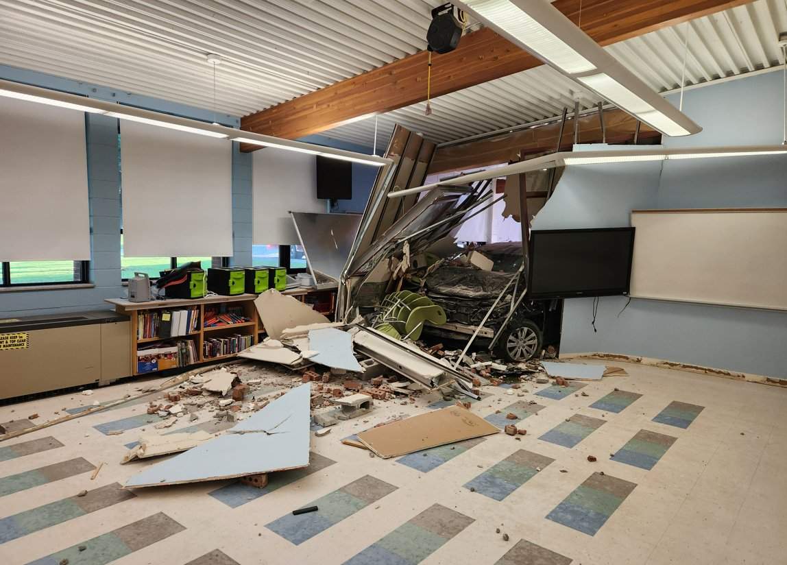 A vehicle partially through a wall in an empty classroom.