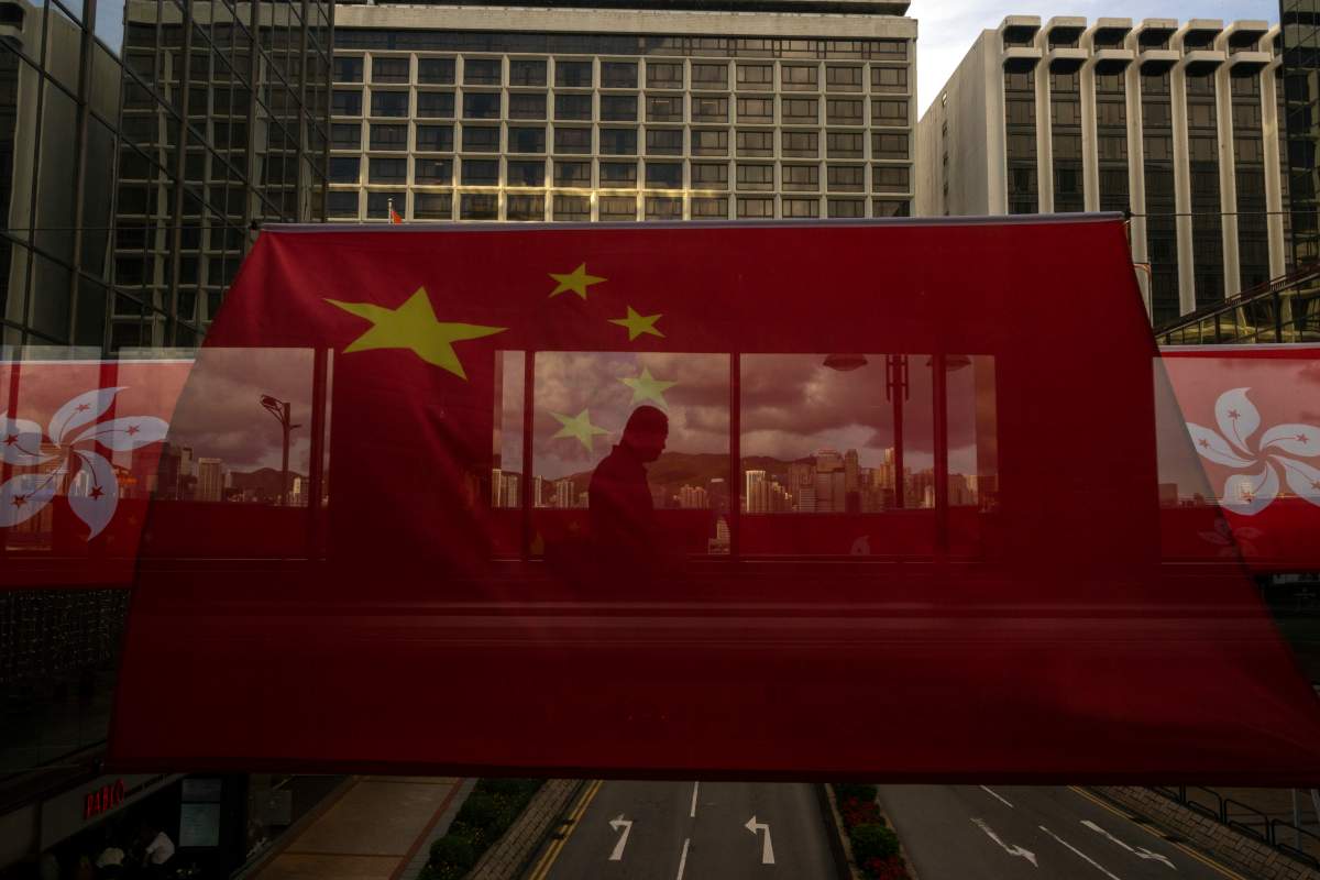 FILE- A pedestrian walking through a footbridge is silhouetted as Chinese and Hong Kong flags are strung to mark the 26th anniversary of the city’s handover from Britain to China in Hong Kong, on June 27, 2023. Hong Kong police arrested another person on Thursday, July 6, accused of d of supporting overseas activists charged with endangering national security, in a further expansion of a government crackdown on dissidents. (AP Photo/Louise Delmotte, File)