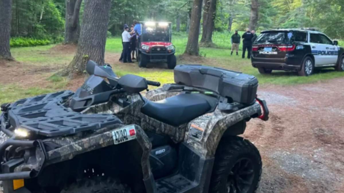 Two ATVs and a police car are parked in a wooded area.
