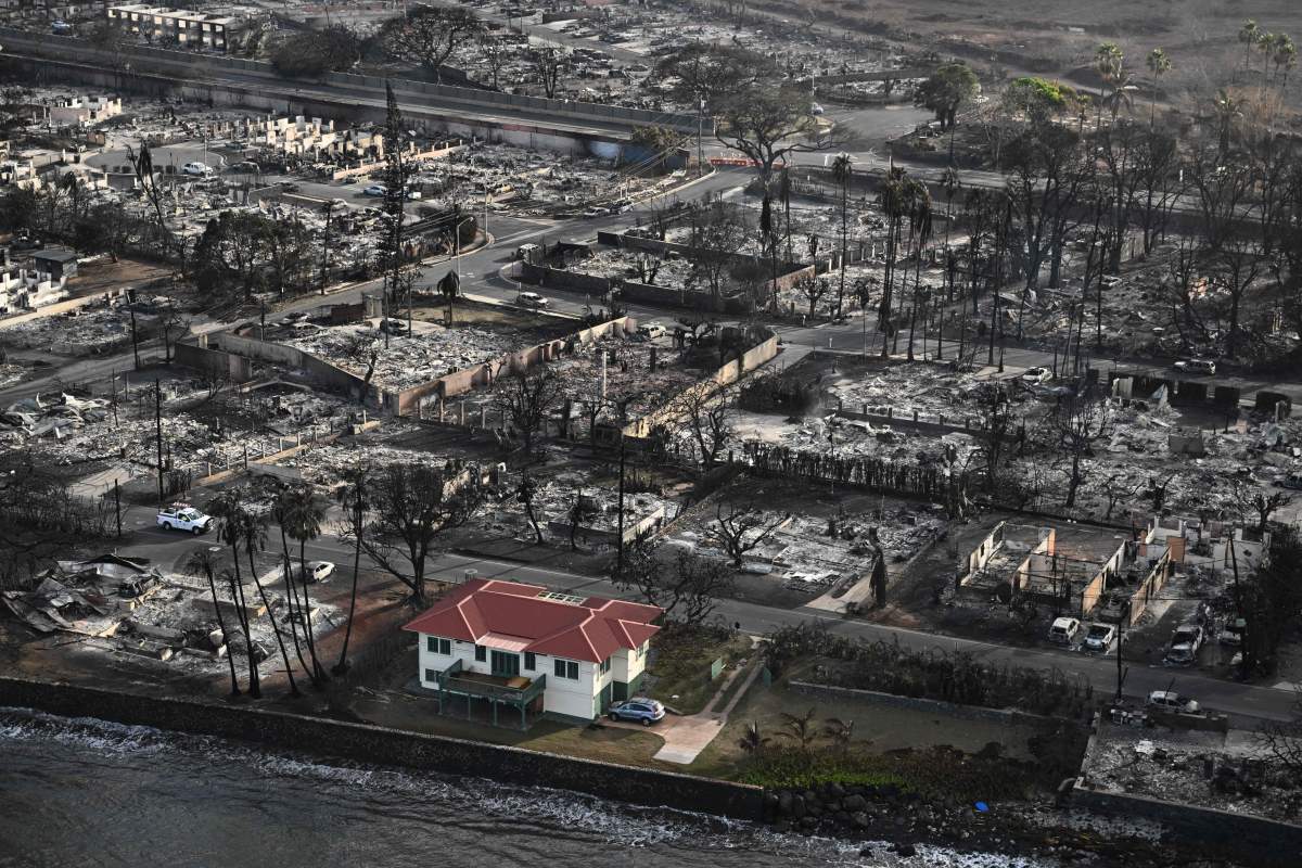 A red-roofed home stands alone amid rubble and ash.