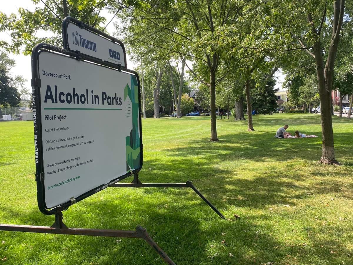 An adult and child sit near the sign for consuming alcohol in public parks in Toronto on Aug. 14, 2023.