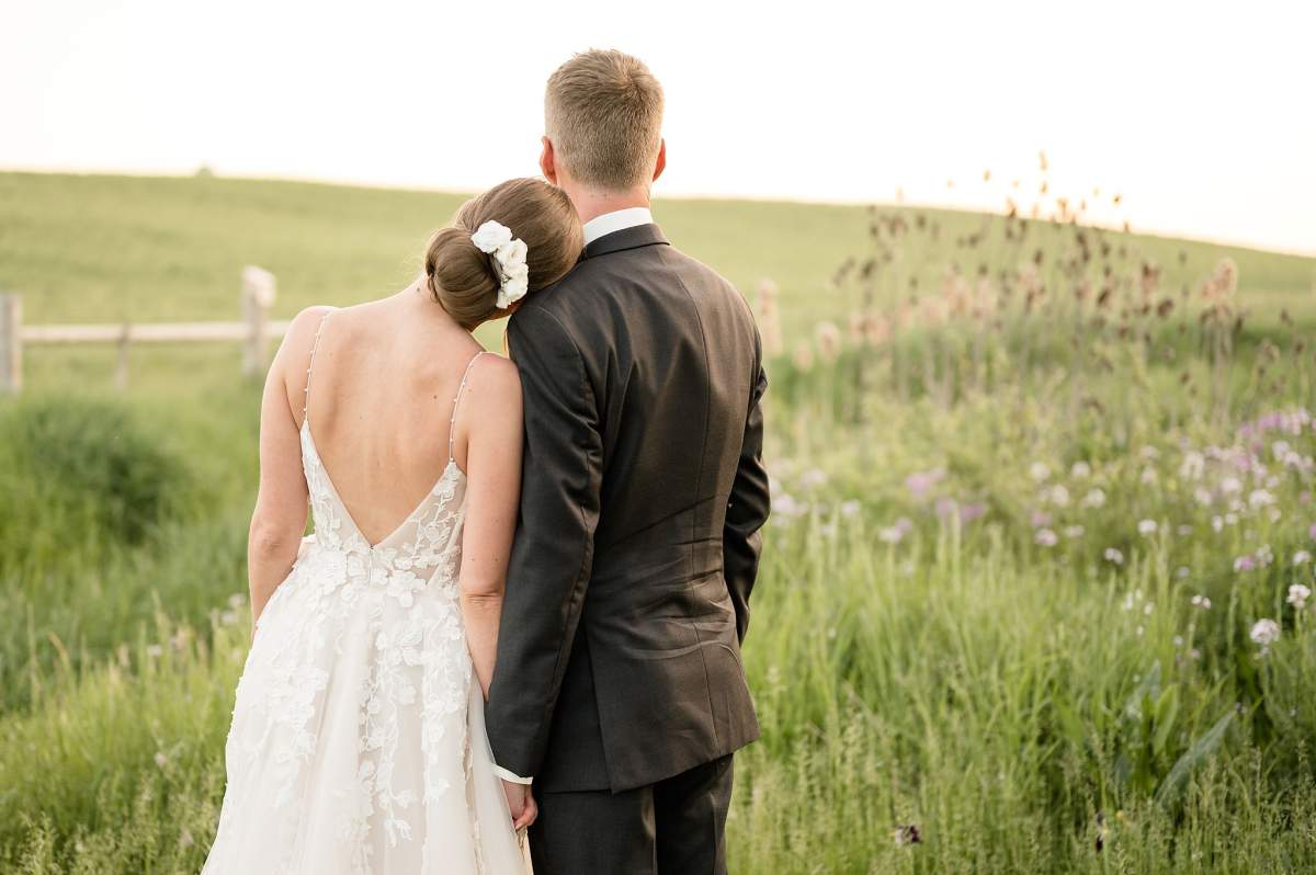 The back of a bride and groom in a field.