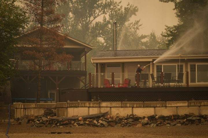 Trevor Manzuik, who was evacuated from his home due to the Lower East Adams Lake wildfire, sprays down his property after returning home by boat, in Scotch Creek, B.C., on Sunday, August 20, 2023.