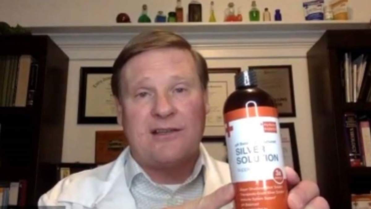 Gordon Hunter Pedersen in a white lab coat, holding a bottle to the camera.