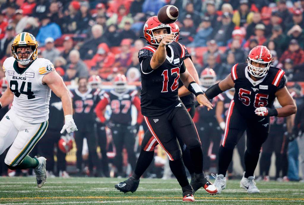 Edmonton Elks defensive lineman Jake Ceresna, left, looks on as Calgary Stampeders quarterback Jake Maier throws the ball during second half CFL football action in Calgary, Alta., Monday, Sept. 4, 2023. The CFL Players' Association says Occupational Health and Safety in Alberta is investigating the CFL's decision to play the Edmonton Elks-Calgary Stampeders game Monday despite smoky conditions in Calgary.