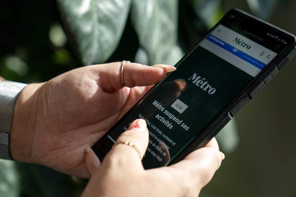 The head of Métro Média says the Quebec newspaper publisher will enter bankruptcy protection this week, ending for good its coverage of local government in parts of the province's two largest cities. A person holds a phone displaying the home page of Metro Media, which reads in French that the company is suspending activities, in Toronto, Friday, Aug. 11, 2023. 