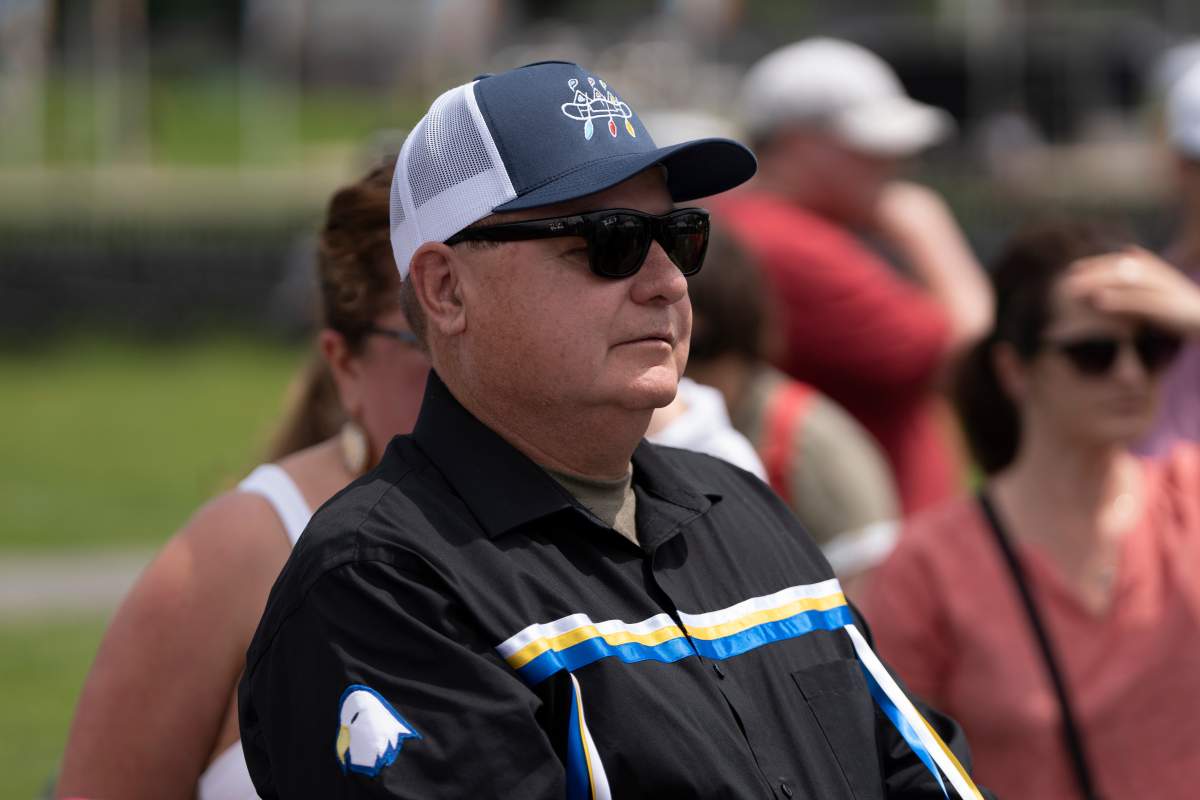 A man wears a ribbon shirt, cap and glasses