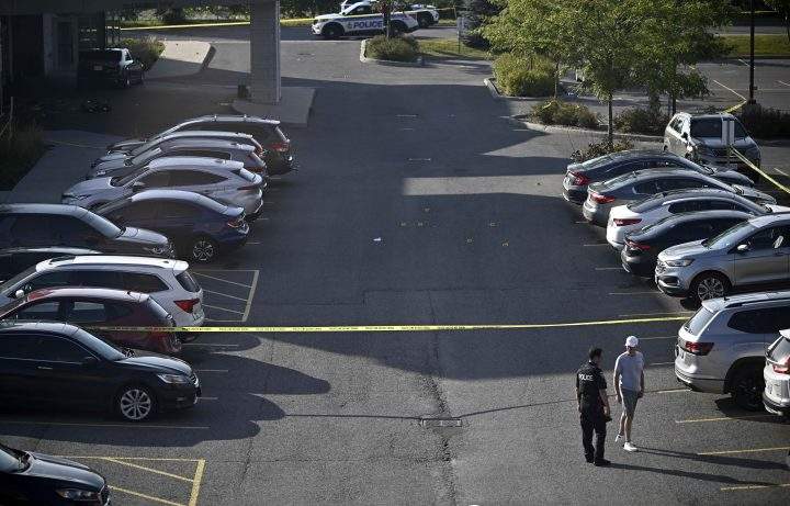 Evidence markers are seen on Sunday in a parking lot as an Ottawa Police officer speaks with a member of the public after a Saturday night shooting at the Infinity Convention Centre left two dead in Ottawa.
