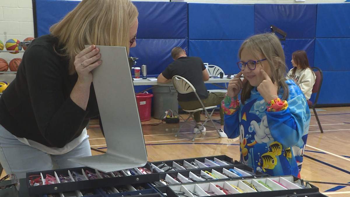 A woman holds a mirror for a child who is trying on glasses
