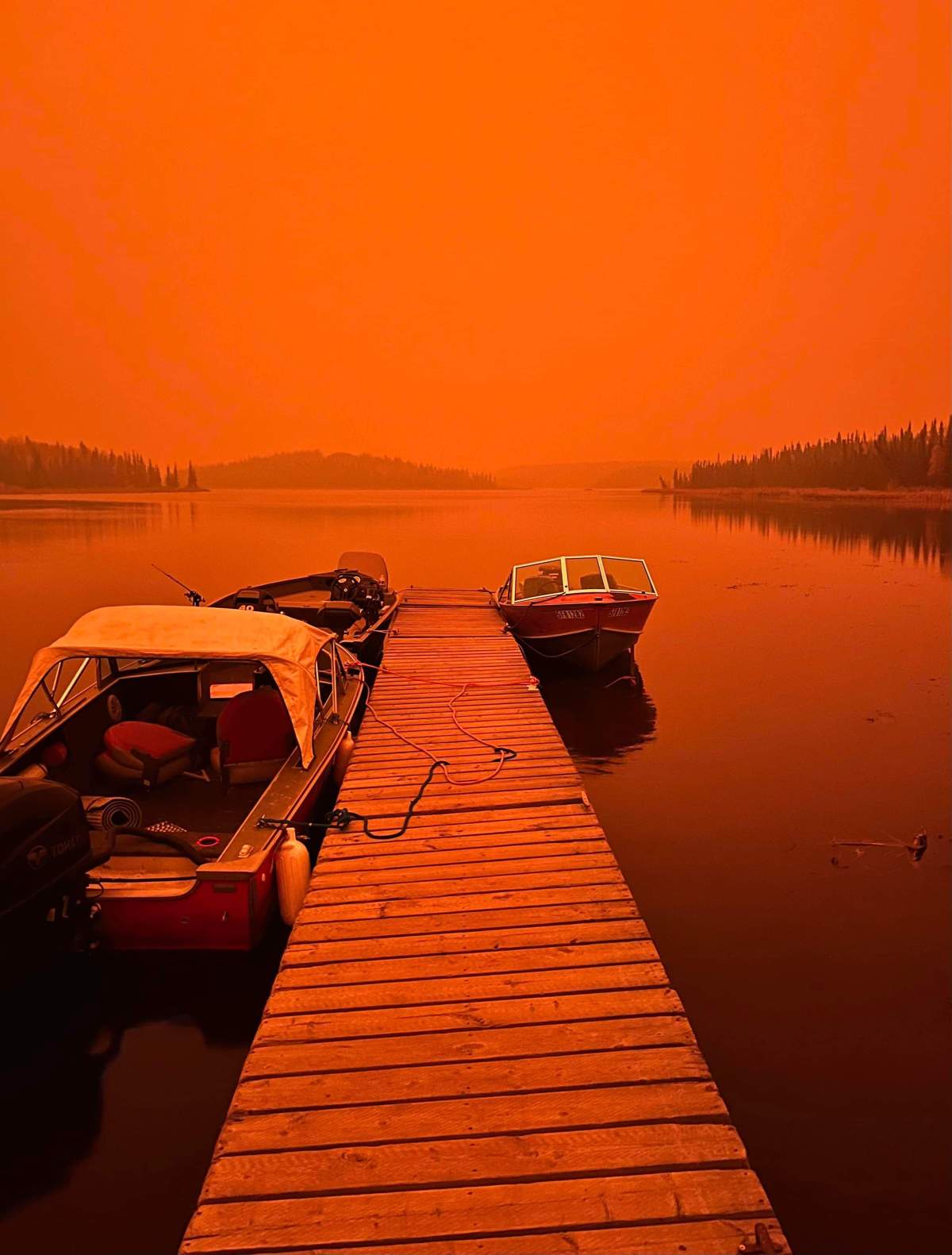 A dock just outside of Yellowknife under a red sky as a wildfire burns nearby.