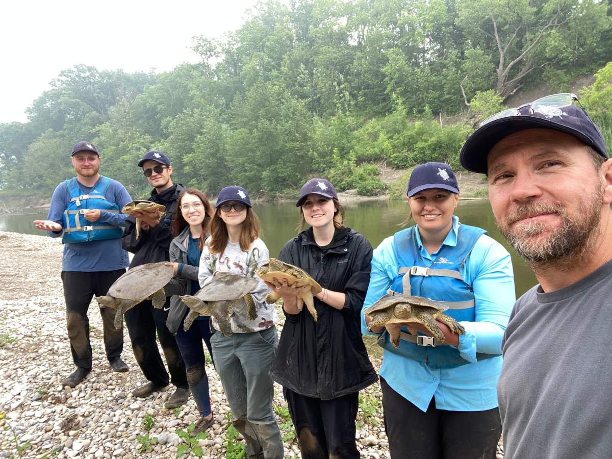 A group of people holding turtles by a river.