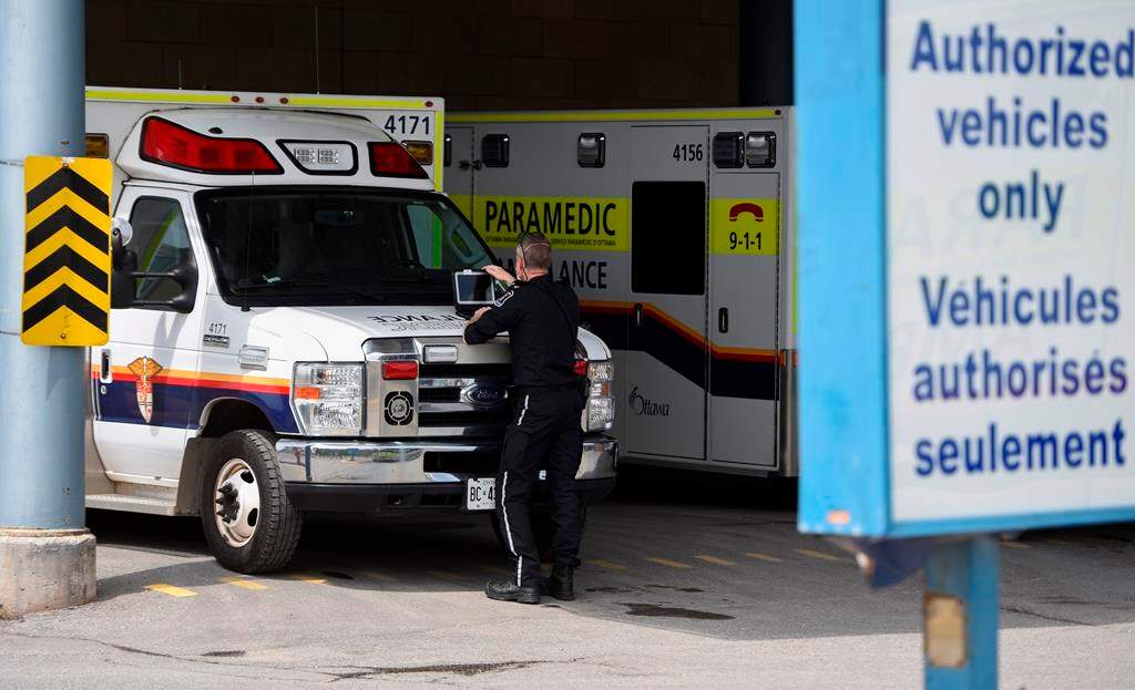 A paramedic works on a laptop on the hood of their ambulance, outside the Emergency Department at the Ottawa Hospital Civic Campus in Ottawa on Monday, May 16, 2022. Ottawa paramedics are seeking provincial approval for a new program that would see some patients with non-urgent concerns taken to hospital in a taxi, in a bid to ease the crushing demands on ambulance crews. THE CANADIAN PRESS/Justin Tang.
