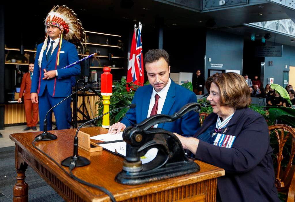 Manitoba Premier Wab Kinew looks on as Adrien Sala, minister of finance, is sworn-in by Lt. Gov. Anita Neville in Winnipeg on Wednesday, Oct. 18, 2023. Manitoba's new NDP government may push back a promise to freeze hydroelectric rates for one year. New numbers from Crown-owned Manitoba Hydro show the utility is now expecting a net loss this year instead of the profit it predicted in the spring. 