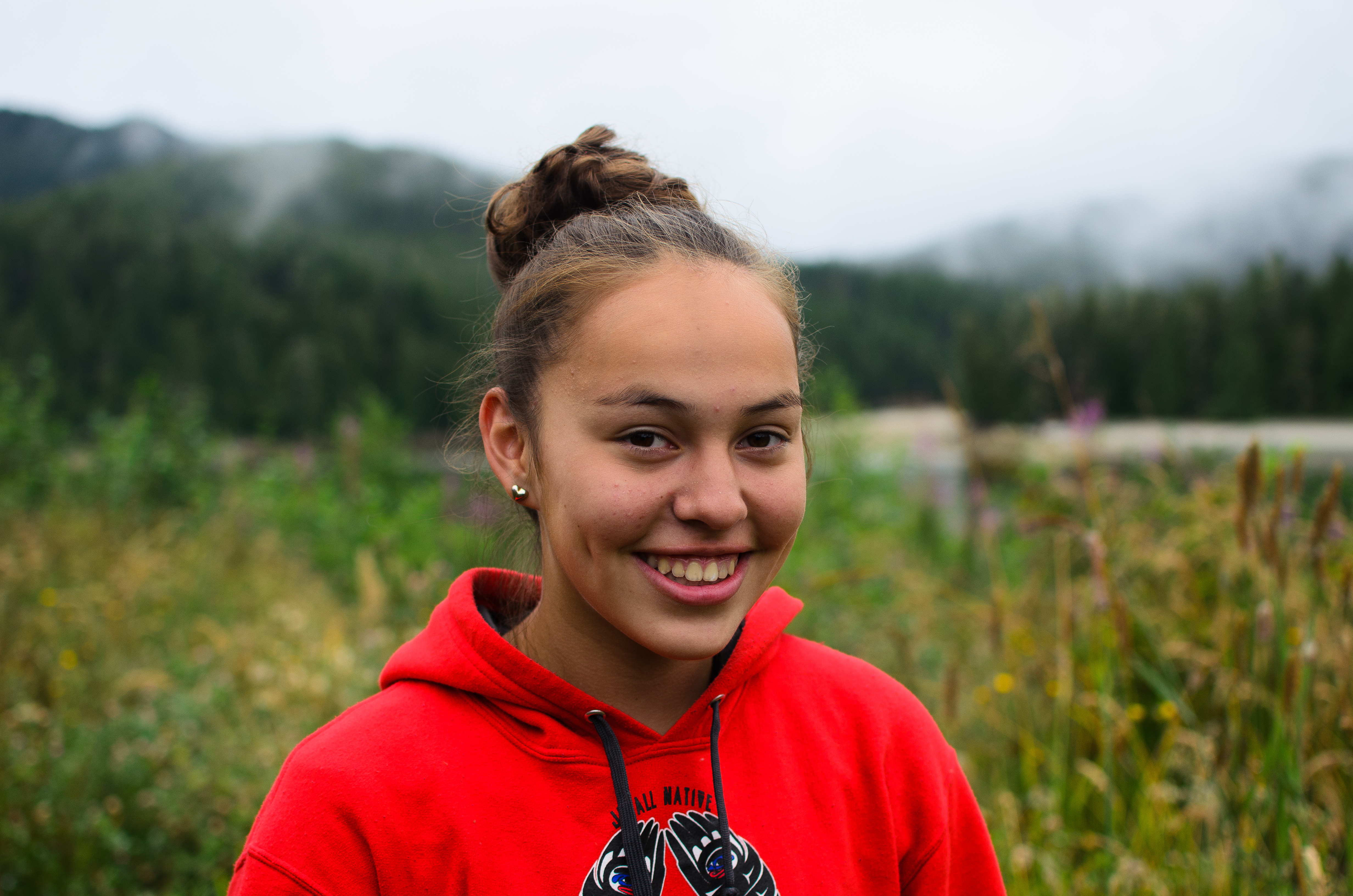 A girl wears a red sweater, smiles at the camer.