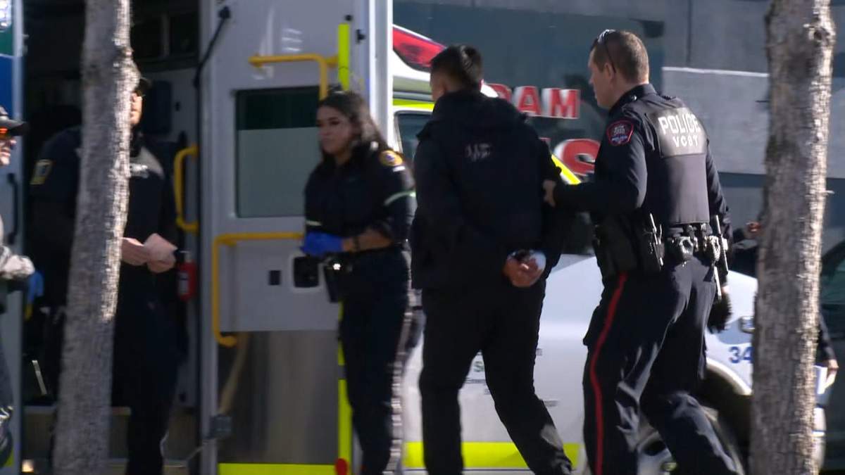Police escort a handcuffed man to an ambulance during the investigation into the shooting of a Calgary Police Service member in a Falconridge strip mall.
