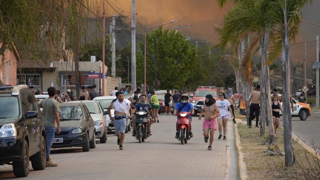 People run away from the rising and approaching flames of wildfire broke out in the resort city of Villa Carlos Paz, Cordoba, Argentina on October 10, 2023.
