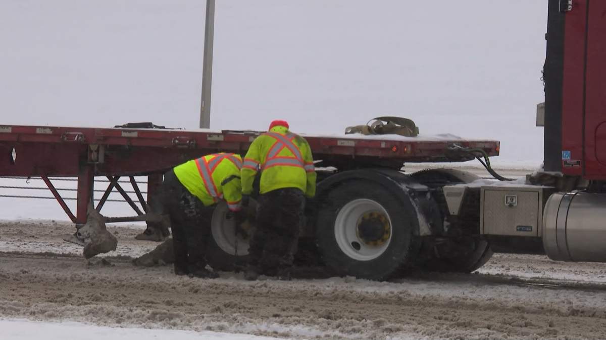 Workers put snow chains on a semi truck along Stoney Trail in Calgary on Oct. 24, 2023.
