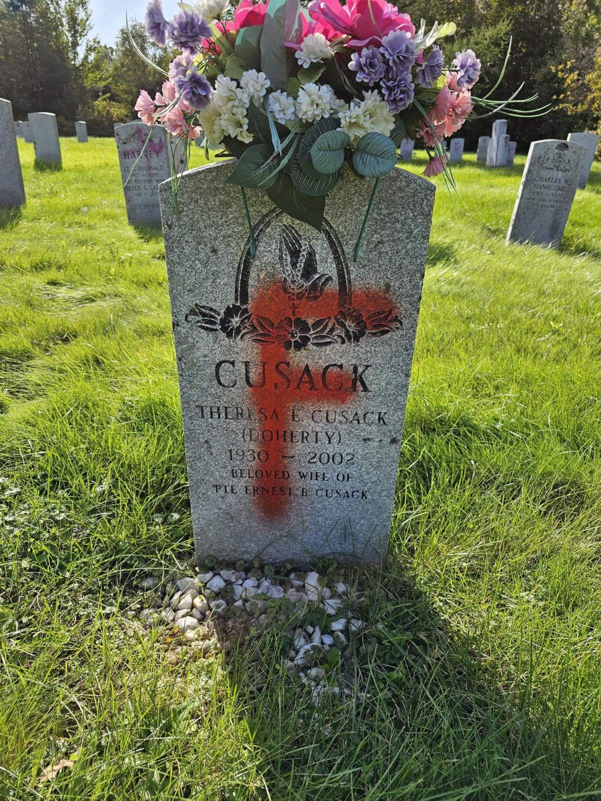 A gravestone with flowers on top has an orange spray painted "F" on it.